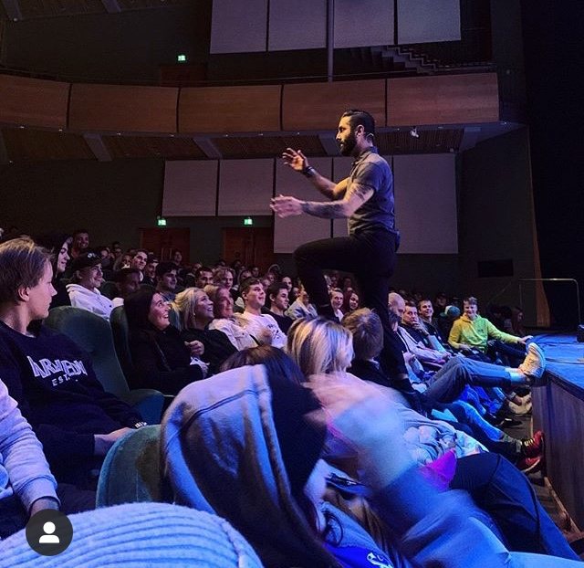 Navid&nbsp;Modiri står uppe bland publikens stolsrader i en salong.